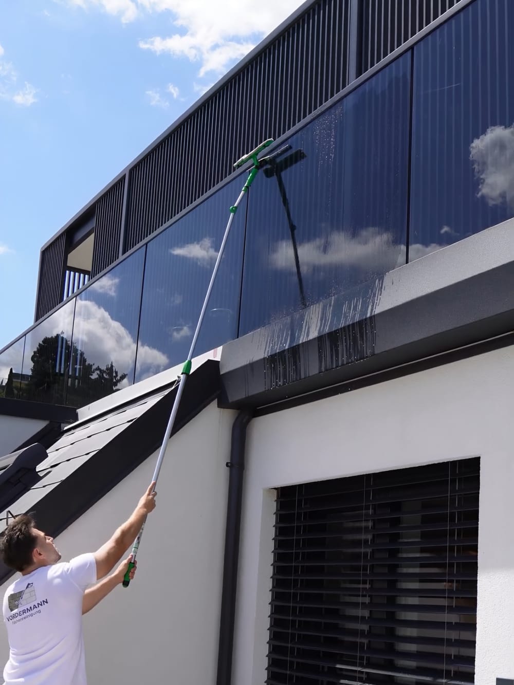 Mitarbeiter reinigt Glasfronten und Fenster mit der Teleskopstange