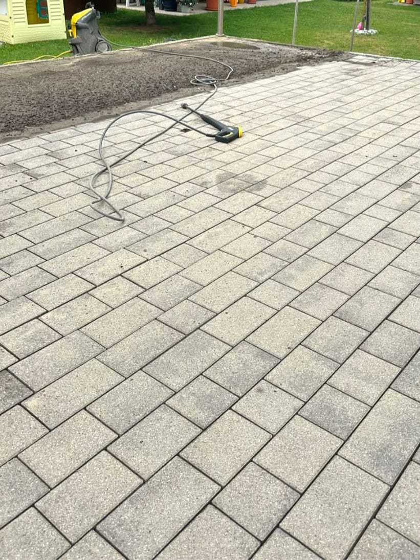 Gepflasterte Gartenfläche während der Reinigung, Hochdruckschlauch liegt bereit